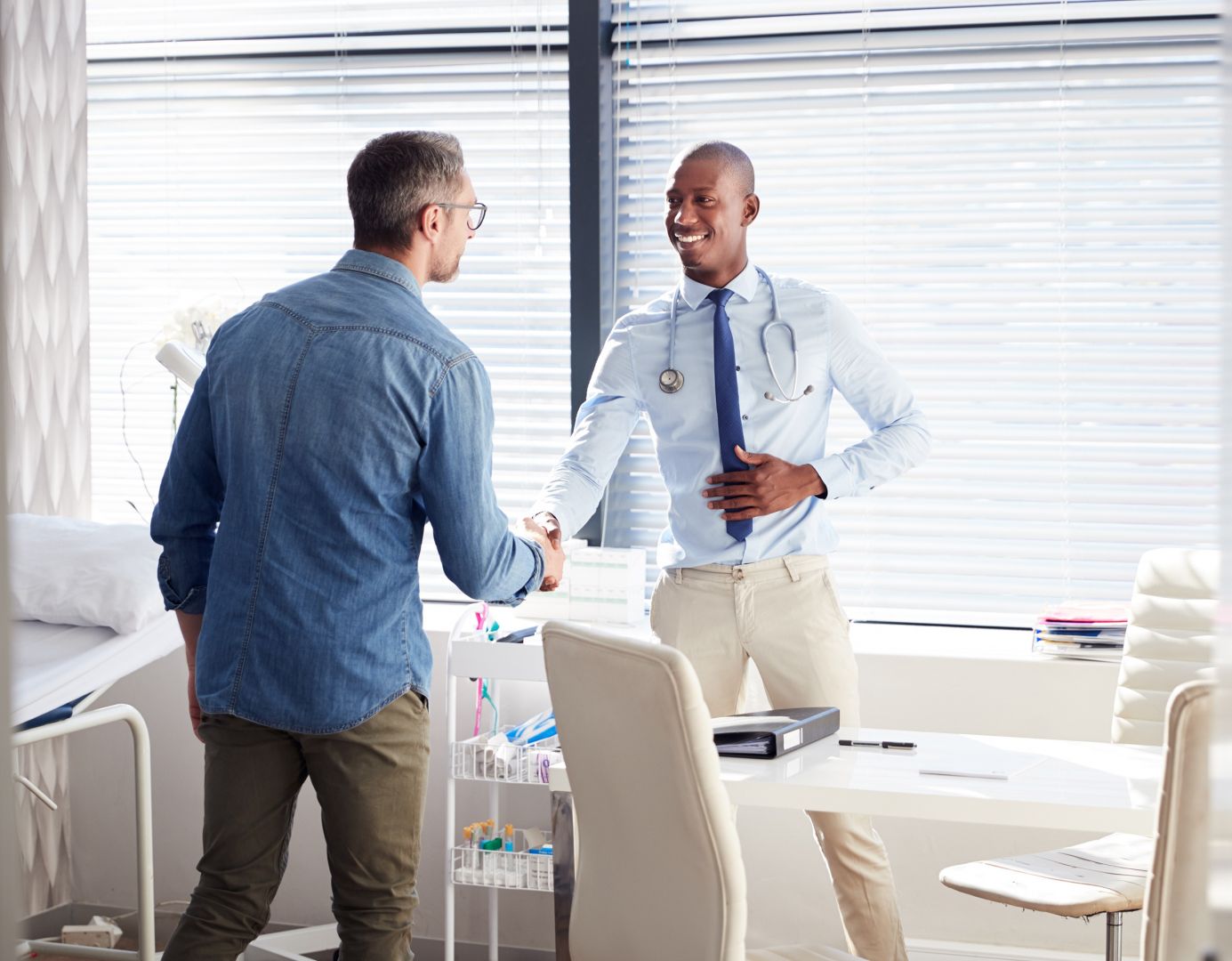 Doctor with sthethescope shaking hands with a patient over a desk before discussing a pre-existing condition