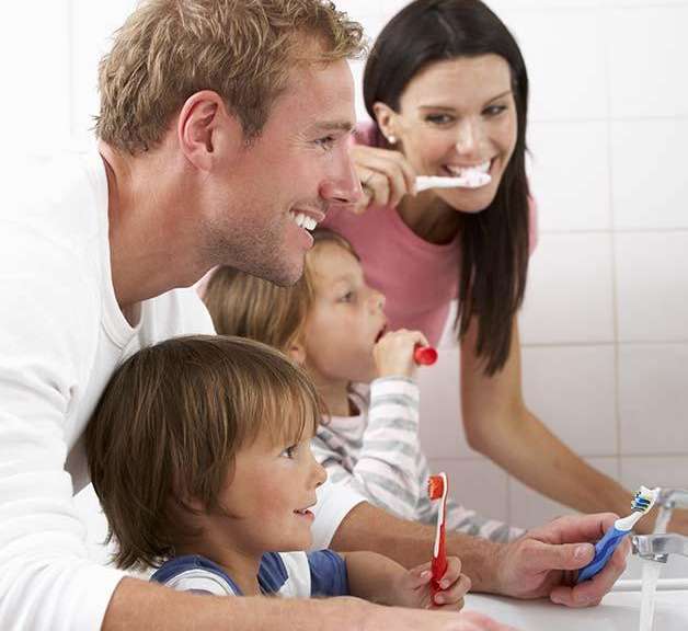 Smiling family brushing teeth together