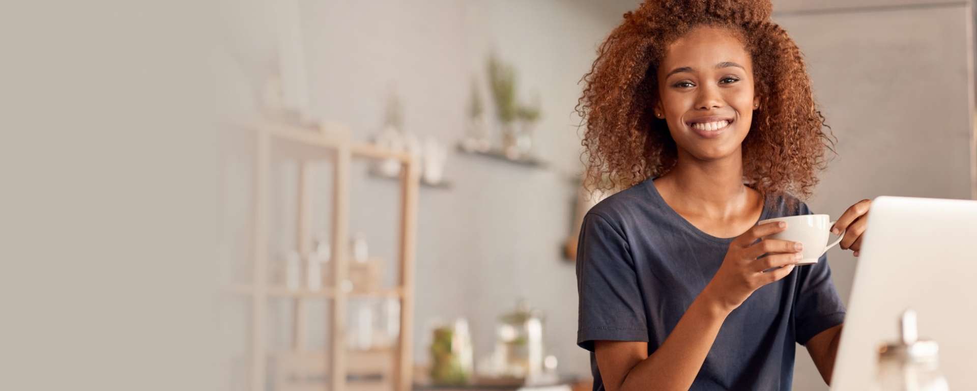 Smiling woman holding a cup of teat in front of a computer » HCi