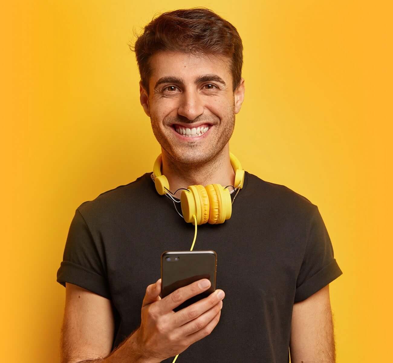 Smiling young man holding a phone and wearing orange head phones, all on an orange background