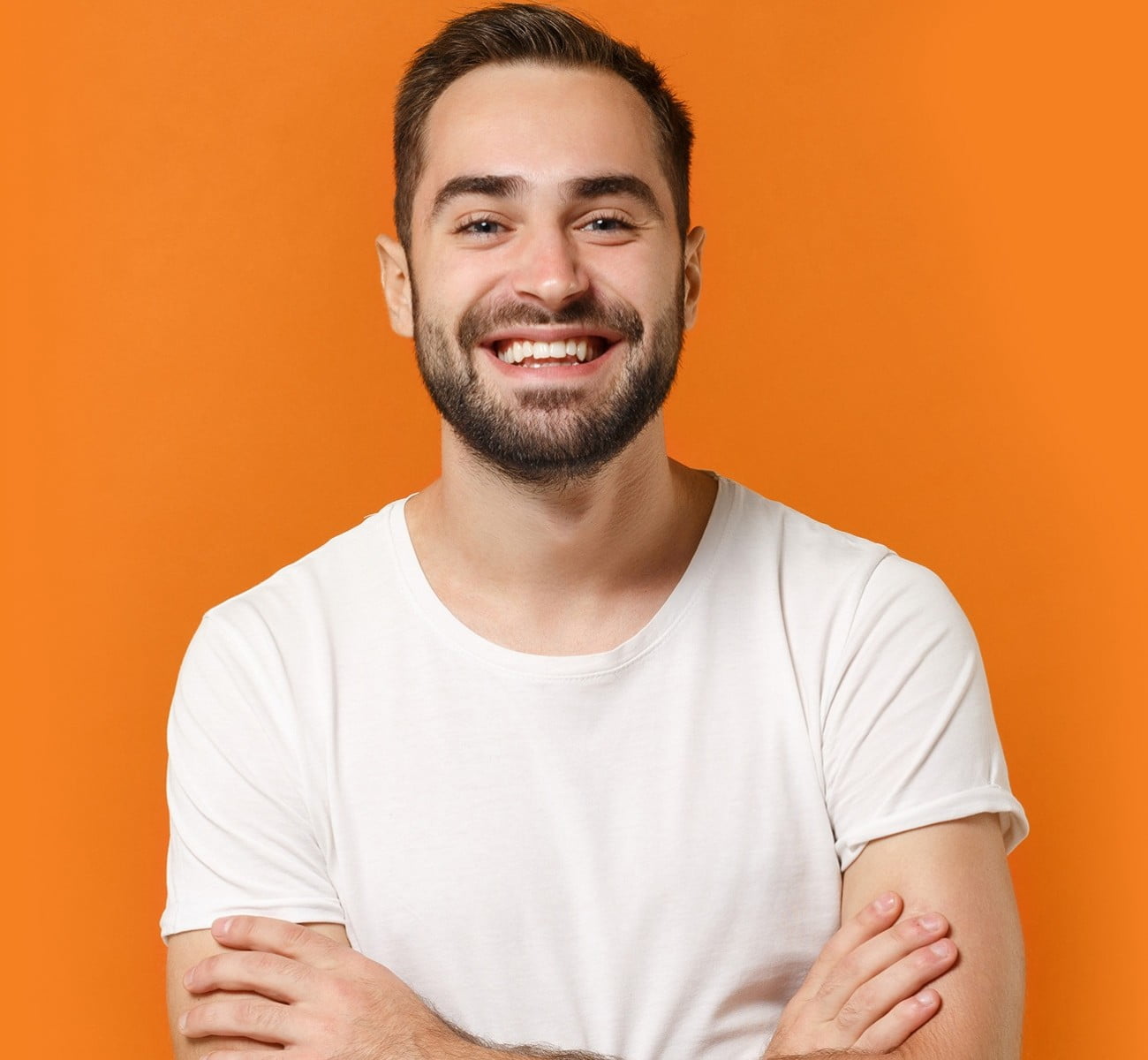 Smiling man with nice teeth and crossed arms on an orange background, happy with his HCi waiting periods » HCi