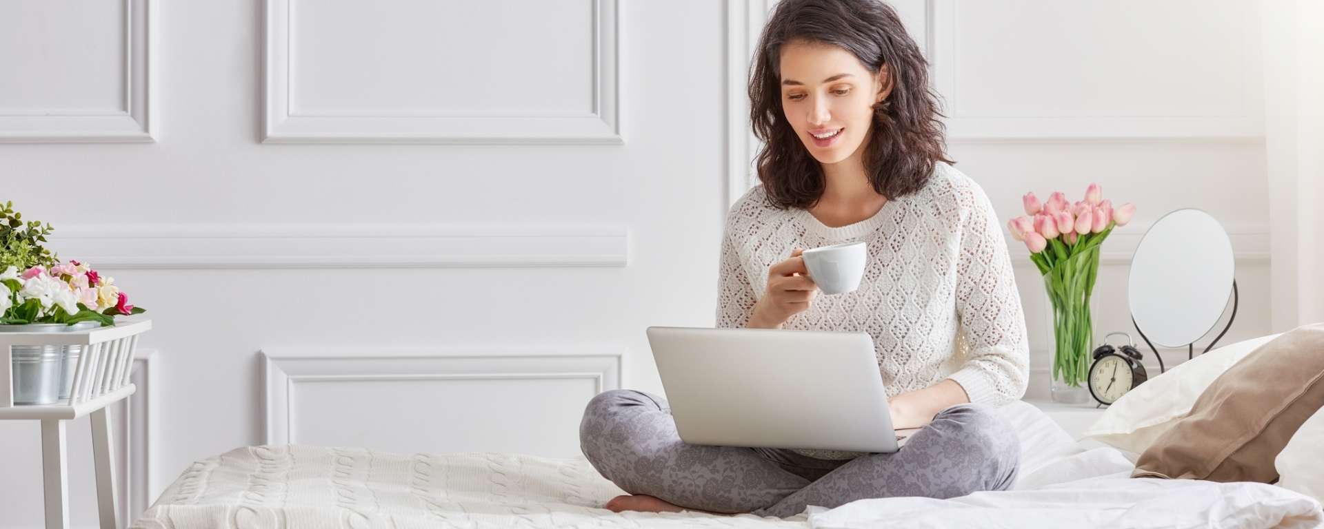 Relaxed woman sitting on a bed with a cup of tea and a laptop