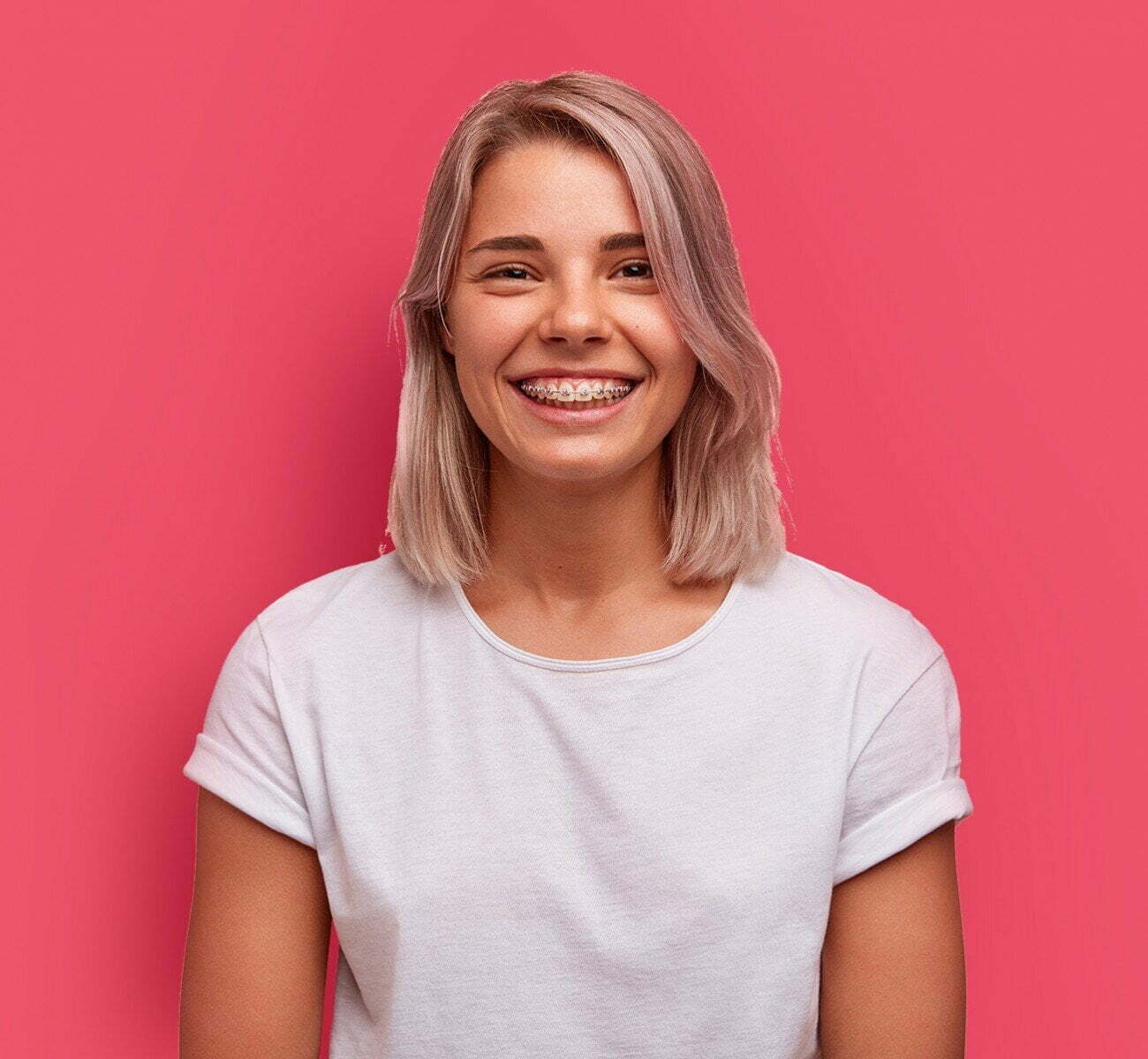 Smiling young woman wearing orthodontic braces on a pink background