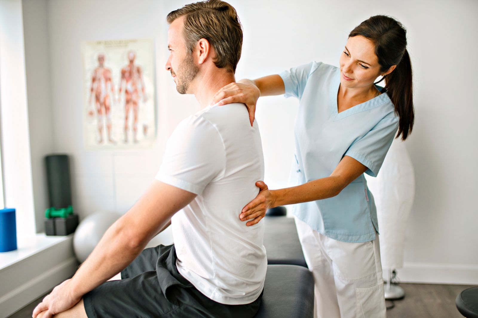 Man sitting on clinician bed while a physio checks his back