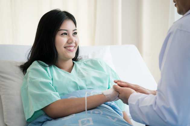 Smiling woman sitting in a hospital bed and holding someone's hands