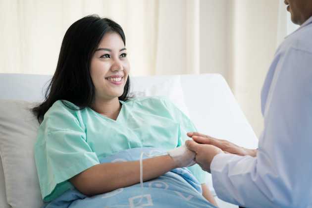 Smiling woman sitting in a hospital bed and holding someone's hands as an inpatient » HCi