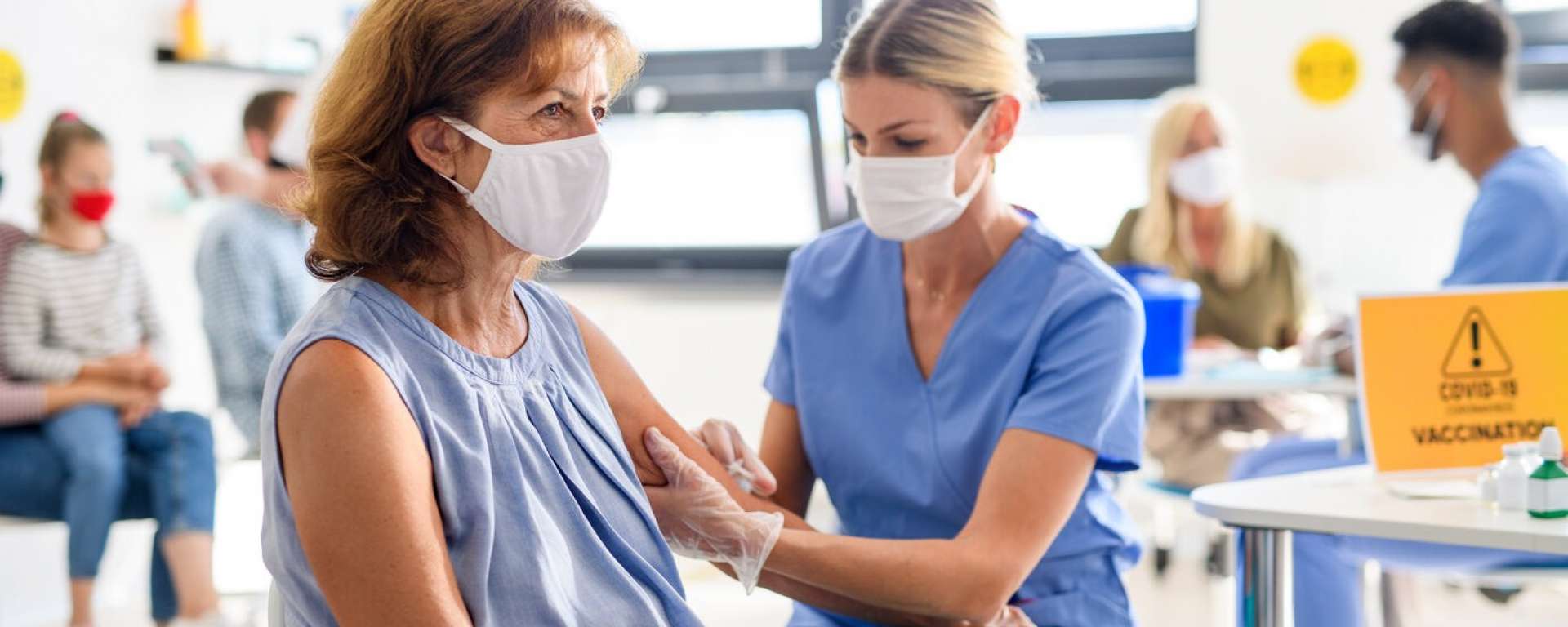 Mature woman in blue getting a vaccination injection from a nurse