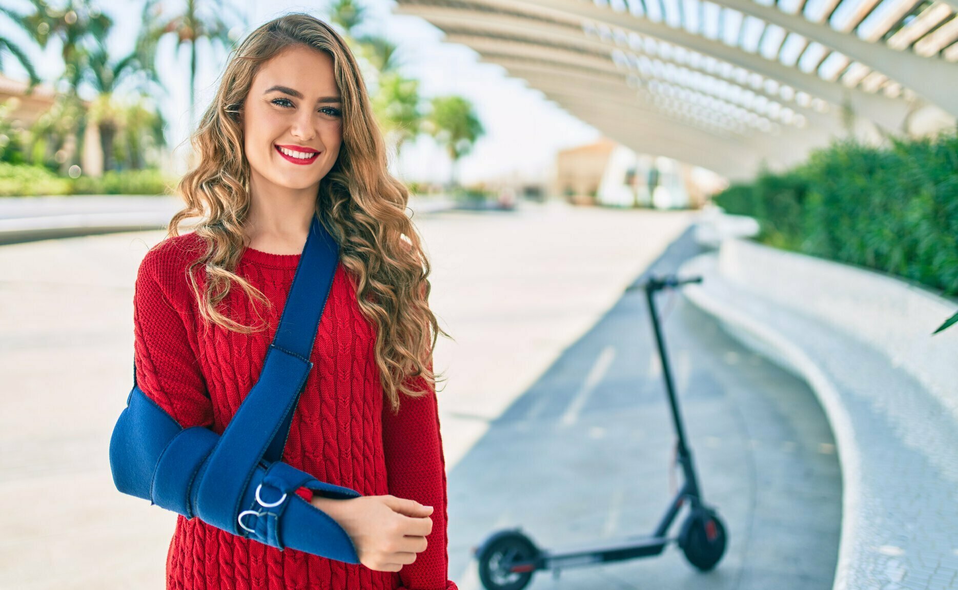 Young woman standing in front of a scooter and wearing a sling after an accident