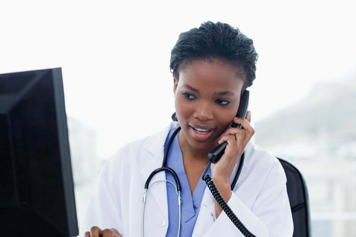 A female cancer support doctor with stethoscope, talking on the phone and looking at a screen » HCi