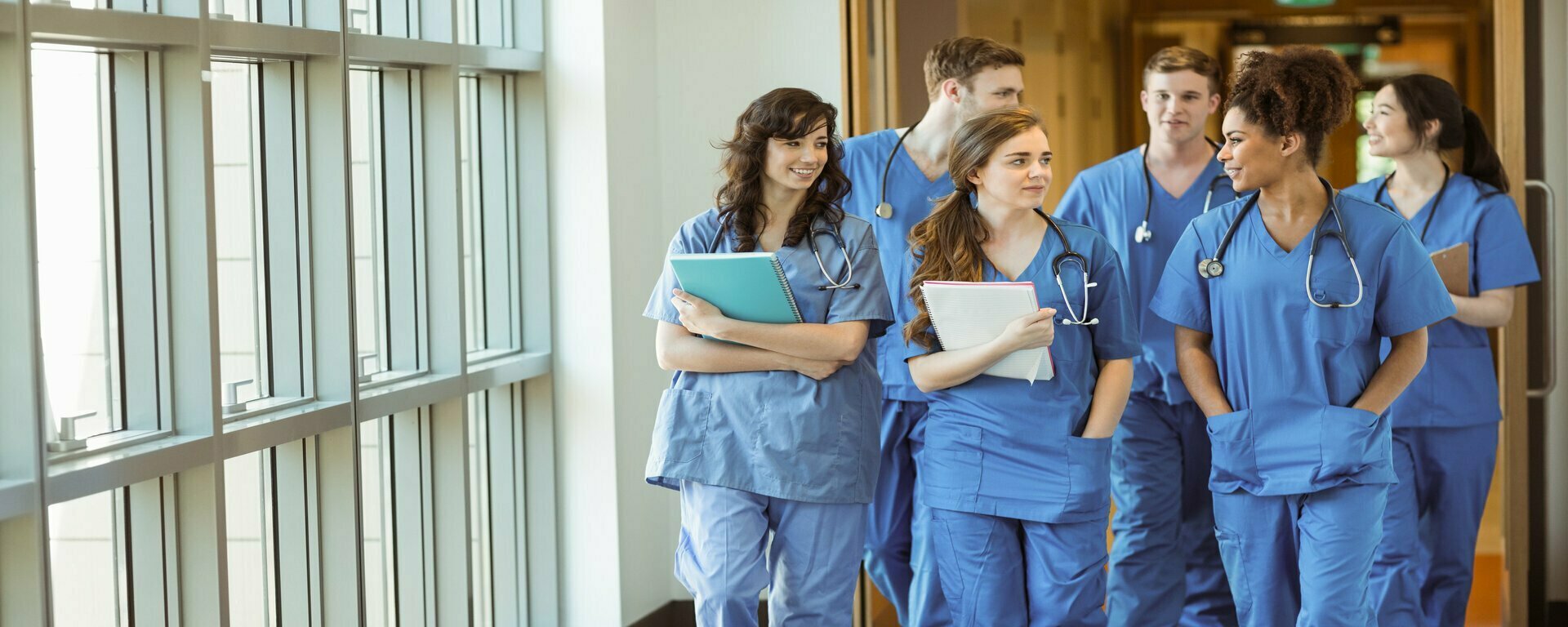 A group of women and men in surgical scrubs walking along a corridor and talking » HCi