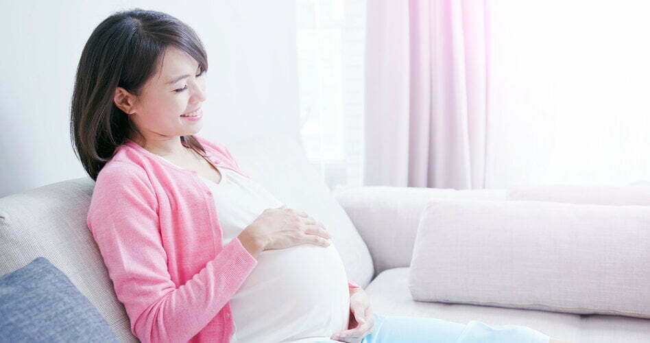 Smiling pregnant woman in a pink cardigan sitting on a couch