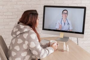Woman sitting with coffee in front of a screen showing a doctor