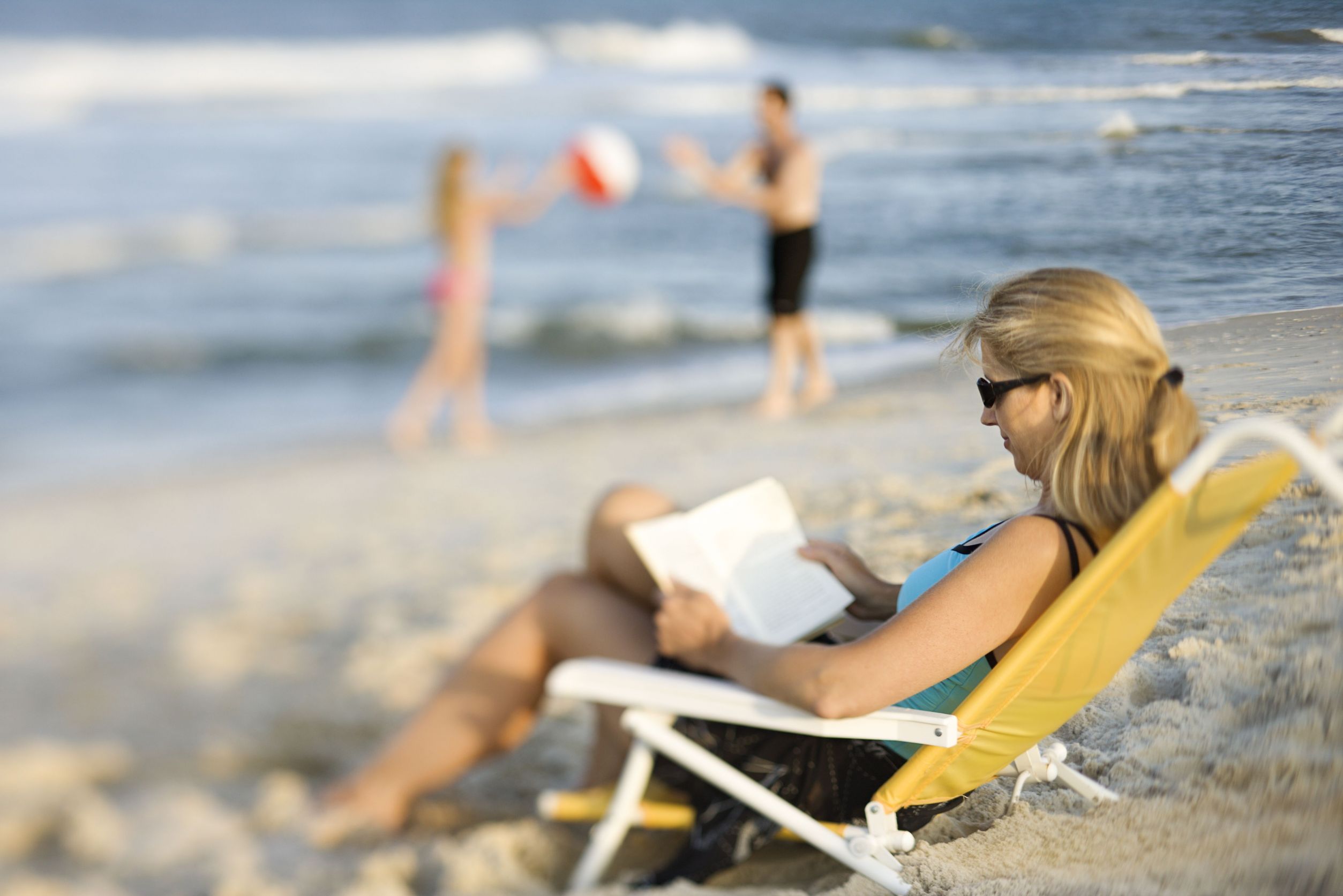 A woman sitting on a reclining chair with a book at the beach » HCi