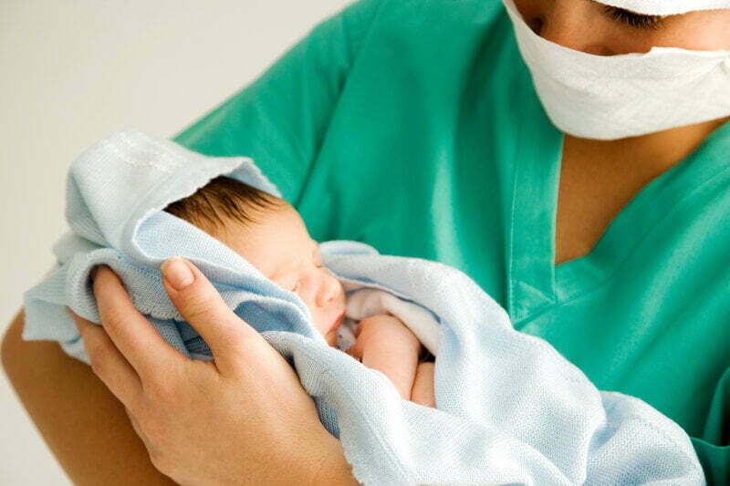 Midwife holding a newborn baby and wearing a mask - HCi Nourish Program » HCi