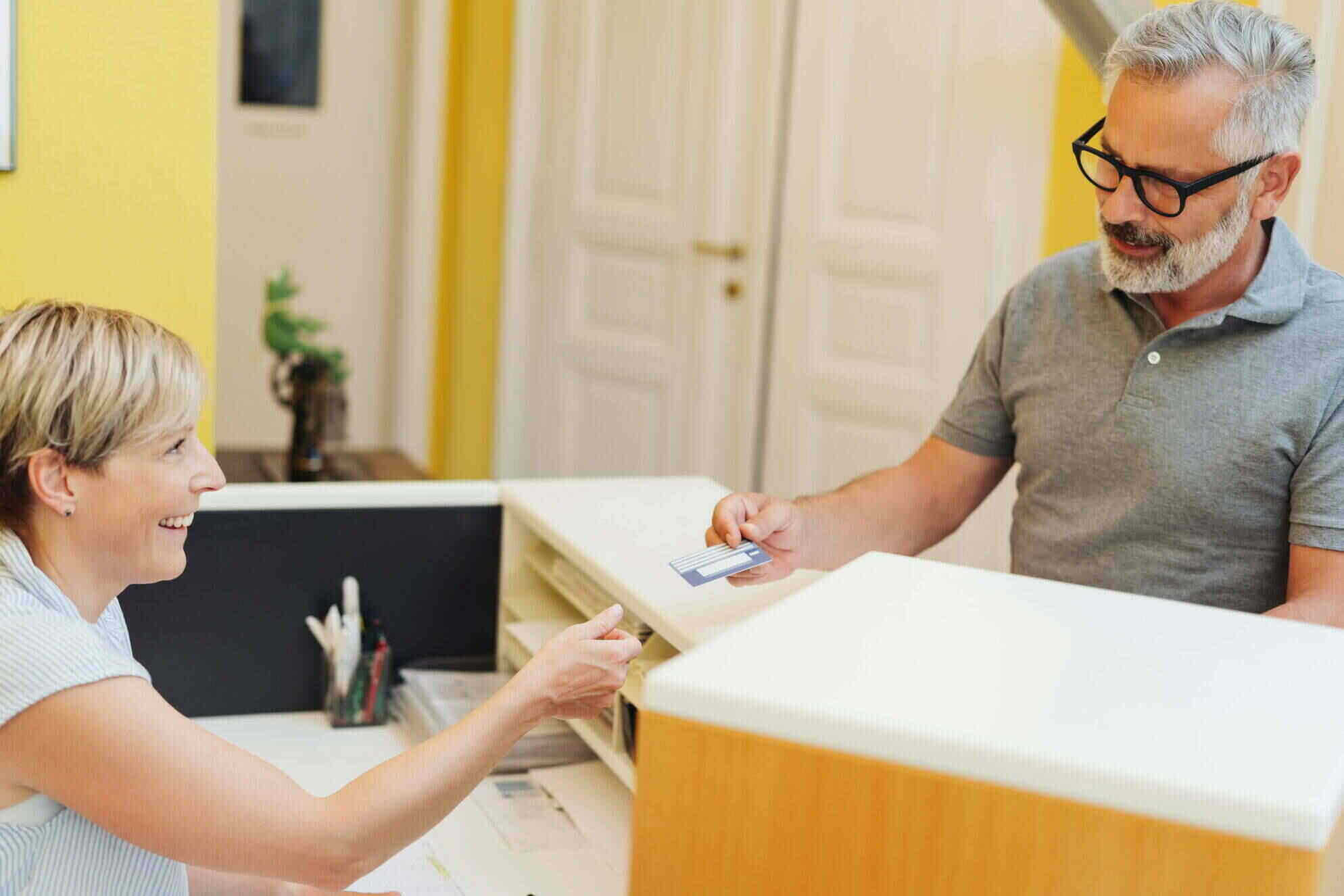 Smiling receptionist accepts credit card from a male patient as an HCi payment option » HCi