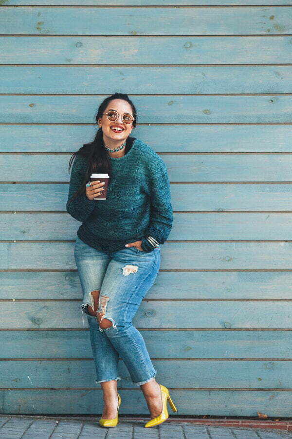 Happy woman holding a coffee cup and leaning against a blue weatherboard wall » HCi