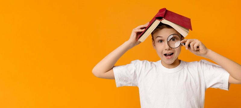 Boy holding a book on his head and a magnifying glass to his eye