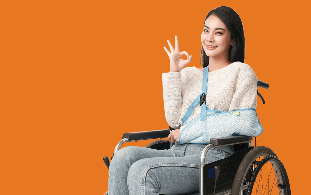 Young woman sitting in a wheelchair, arm in a sling, smiling and making an okay sign