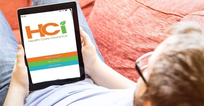 Man reclining on a couch, holding a table showing the HCi claiming app » HCi